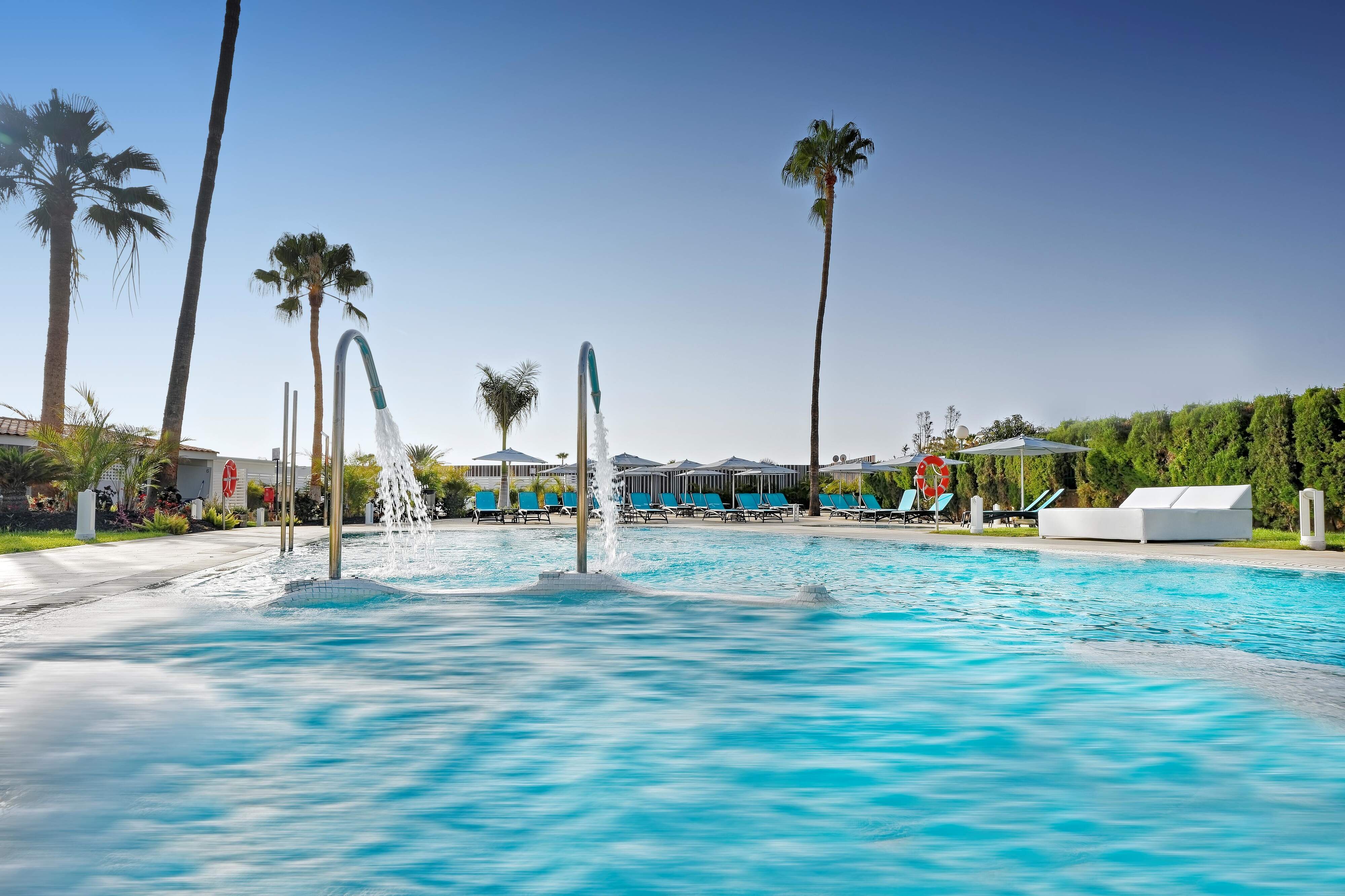 Piscine entourée de transats bleus et palmiers, Relaxia