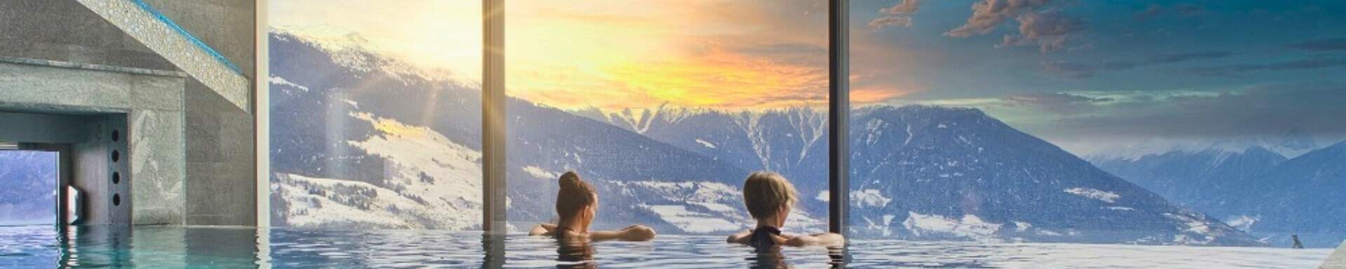 Deux femmes de dos dans une piscine, admirant la vue sur les montagnes enneigées dans un centre de bien-être de luxe