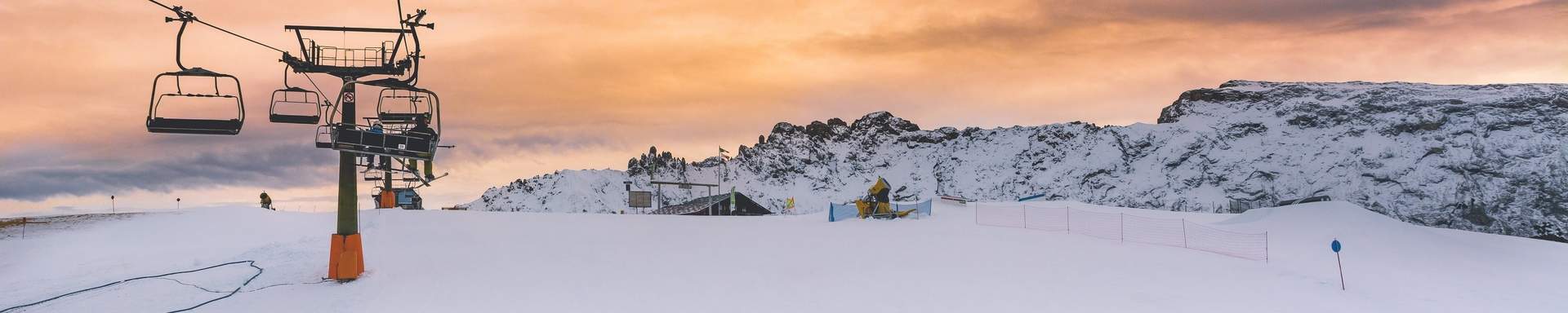 Vue sur des remontées mécaniques, des montagnes enneigées et un coucher de soleil 
