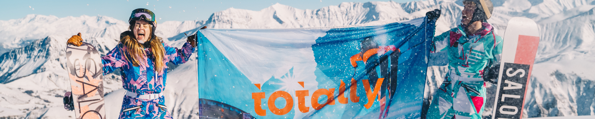 Un homme et une femme rient dans la neige avec un snowboard à la main et brandissent le drapeau de Totally Snow