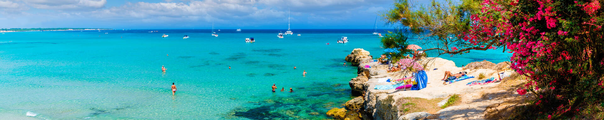 Plage avec sa jetée de rochers donnant sur eaux cristallines et bougainvillier fuschia
