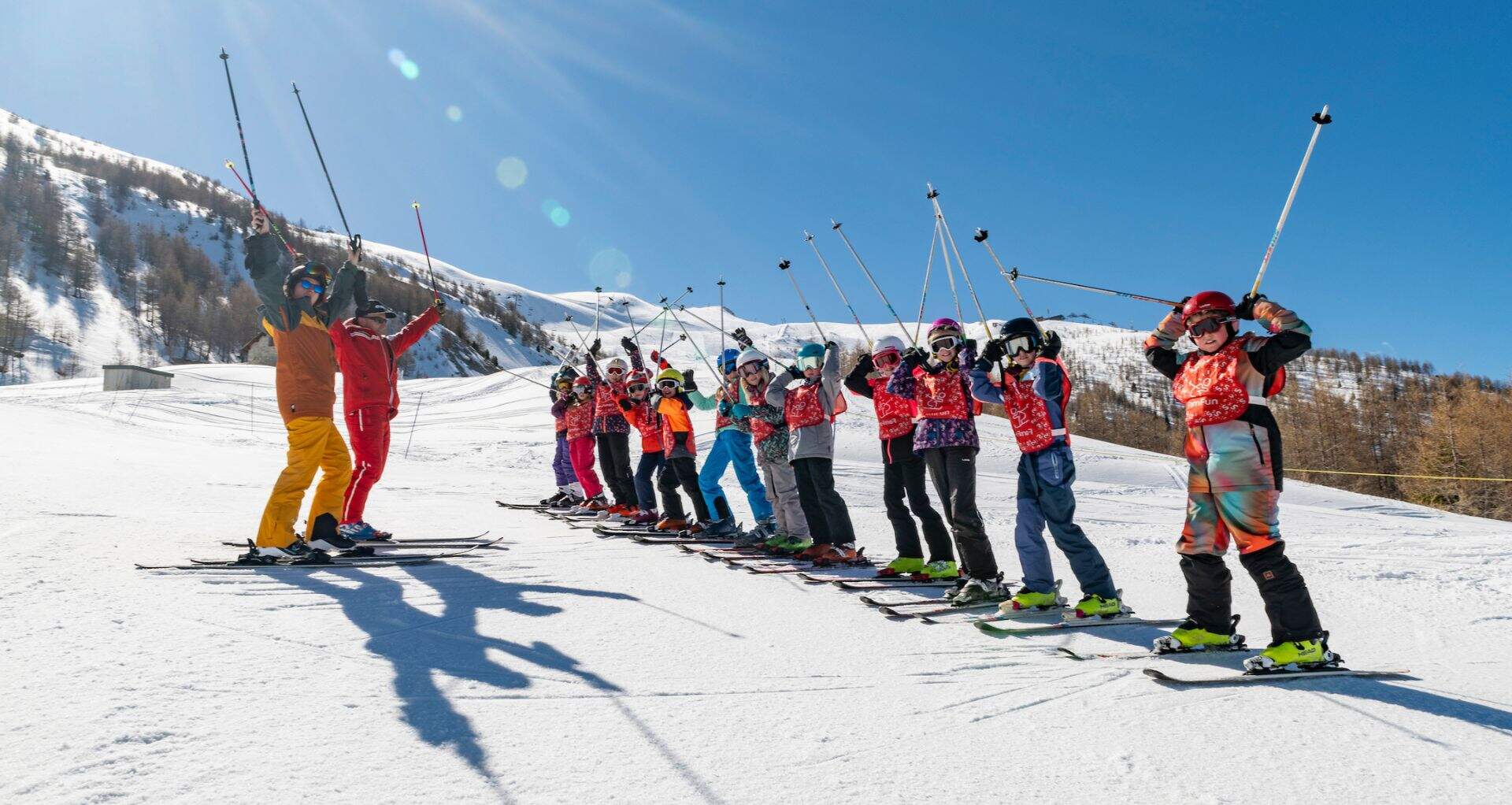 skiklasje met kinderen en twee leraren op skies in de sneeuw houden hun skistokken in de lucht 