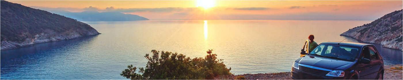 persoon bij auto aan kust met uitzicht over zee tijdens zonsondergang