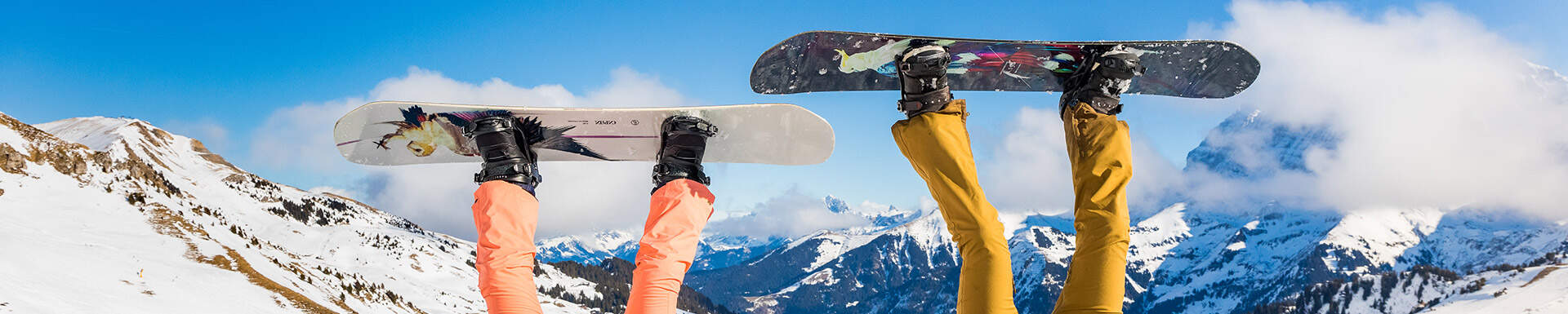 benen van twee mensen op een skipiste die skikleding en een snowboard aan hun voeten dragen 