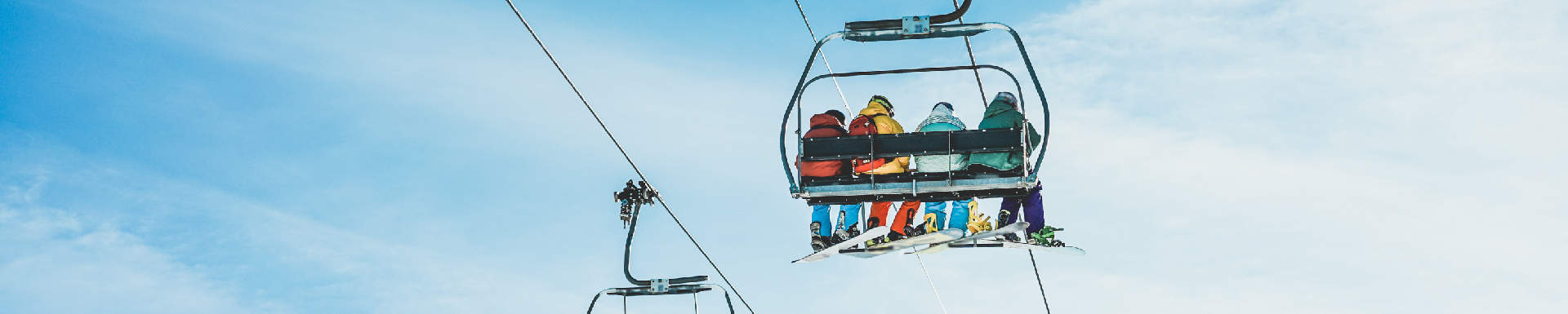 vier mensen van achteren gefotografeerd zittend in een stoeltjes skilift met gekleurde skikleding aan
