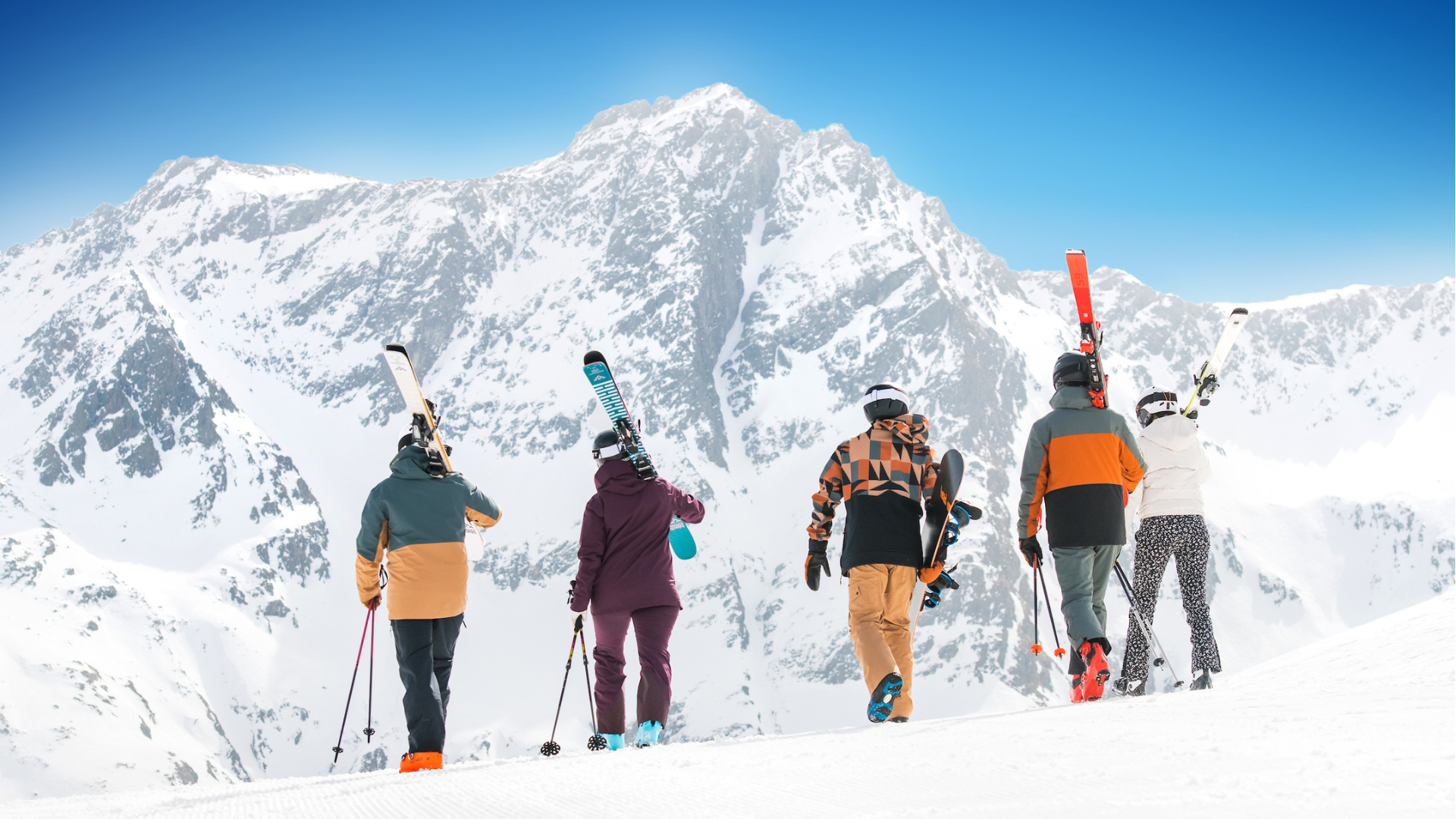 lopende groep skiers van achteren gefotografeerd op skipiste met skimateriaal op hun schouder