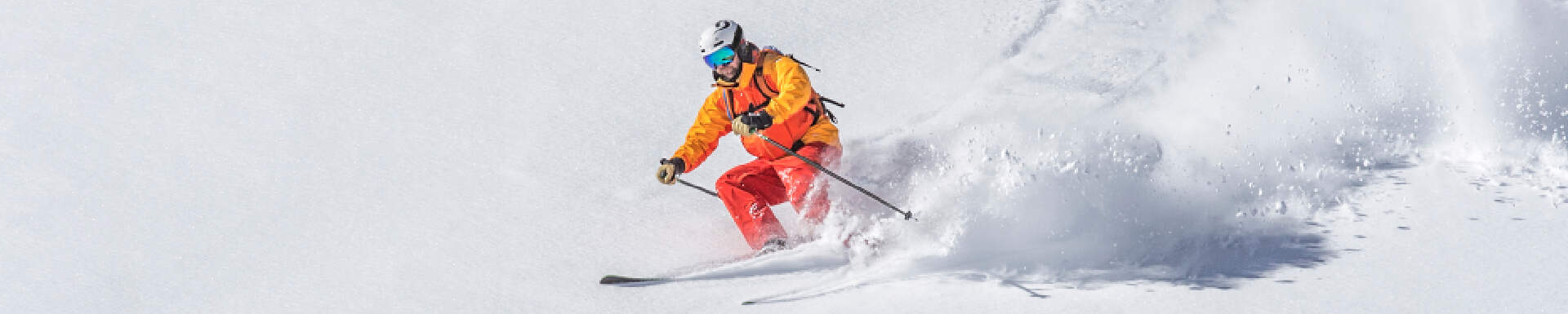 skier met geel oranje skikleding die met gebogen knieen van de berg afskiet 