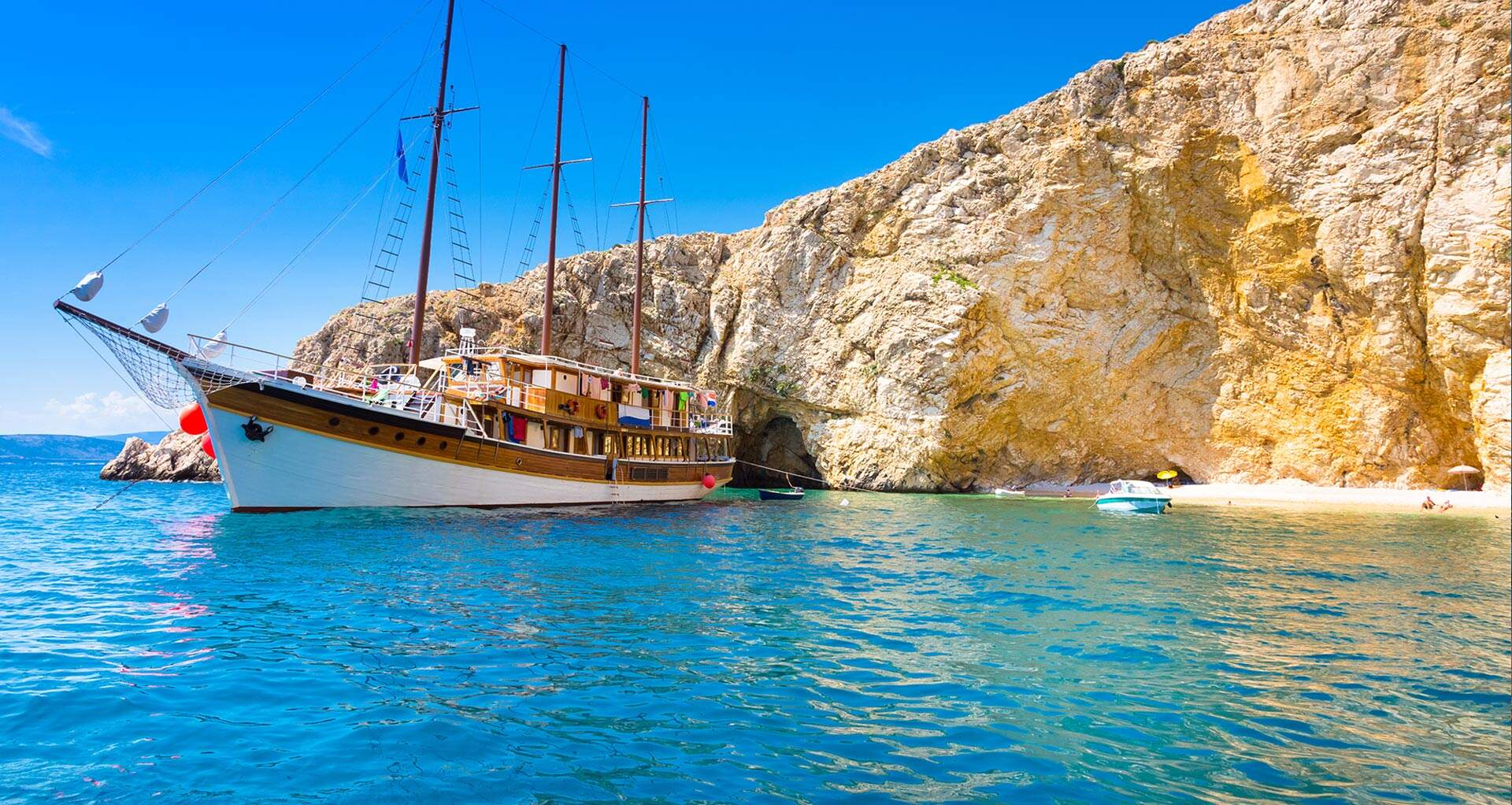 zeilboot in helderblauw water en gele rotspartijen voor de kust van kroatie