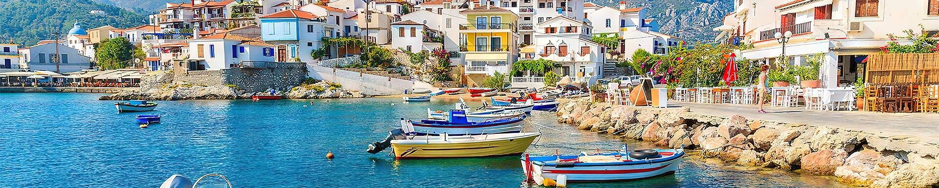 gekleurde roeibootjes aan rotsachtige kustlijn van cyprus met witte vakantiehuisjes op de achtergrond