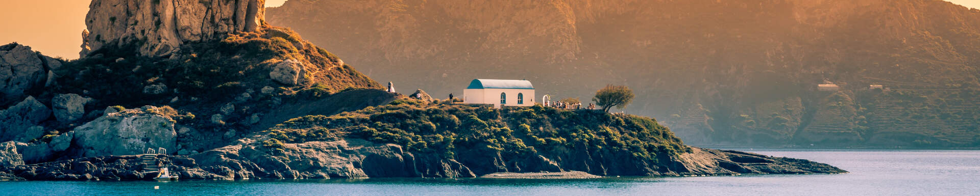 Rotsformatie met klein kerkje langs de kust van Kos in de avondzon