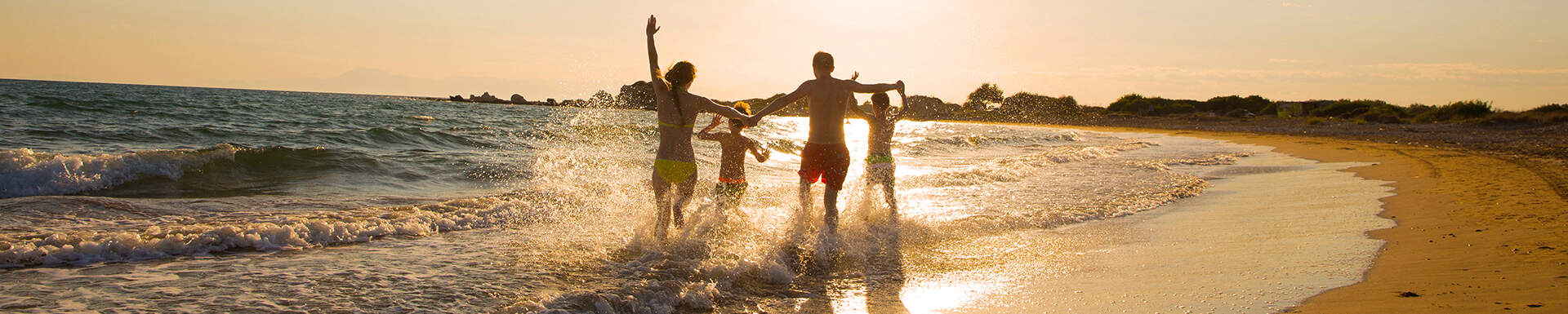 man en vrouw met twee kinderen rennend langs de branding aan zee tijdens zonsondergang