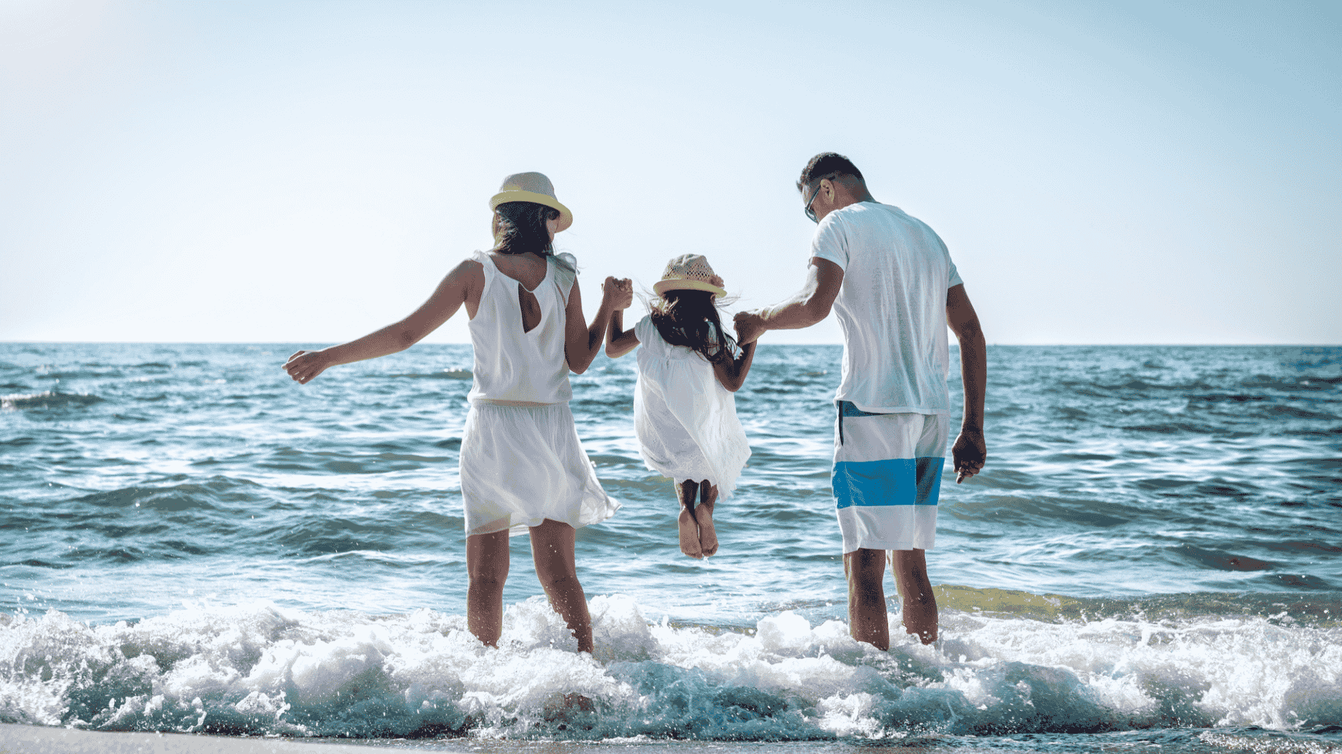 Vader en moeder tillen meisje op langs de branding van zee