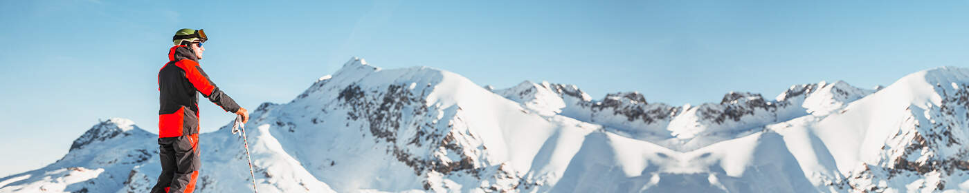 man in skikleding en stokken in zijn hand uitkijkend over besneeuwde bergtoppen