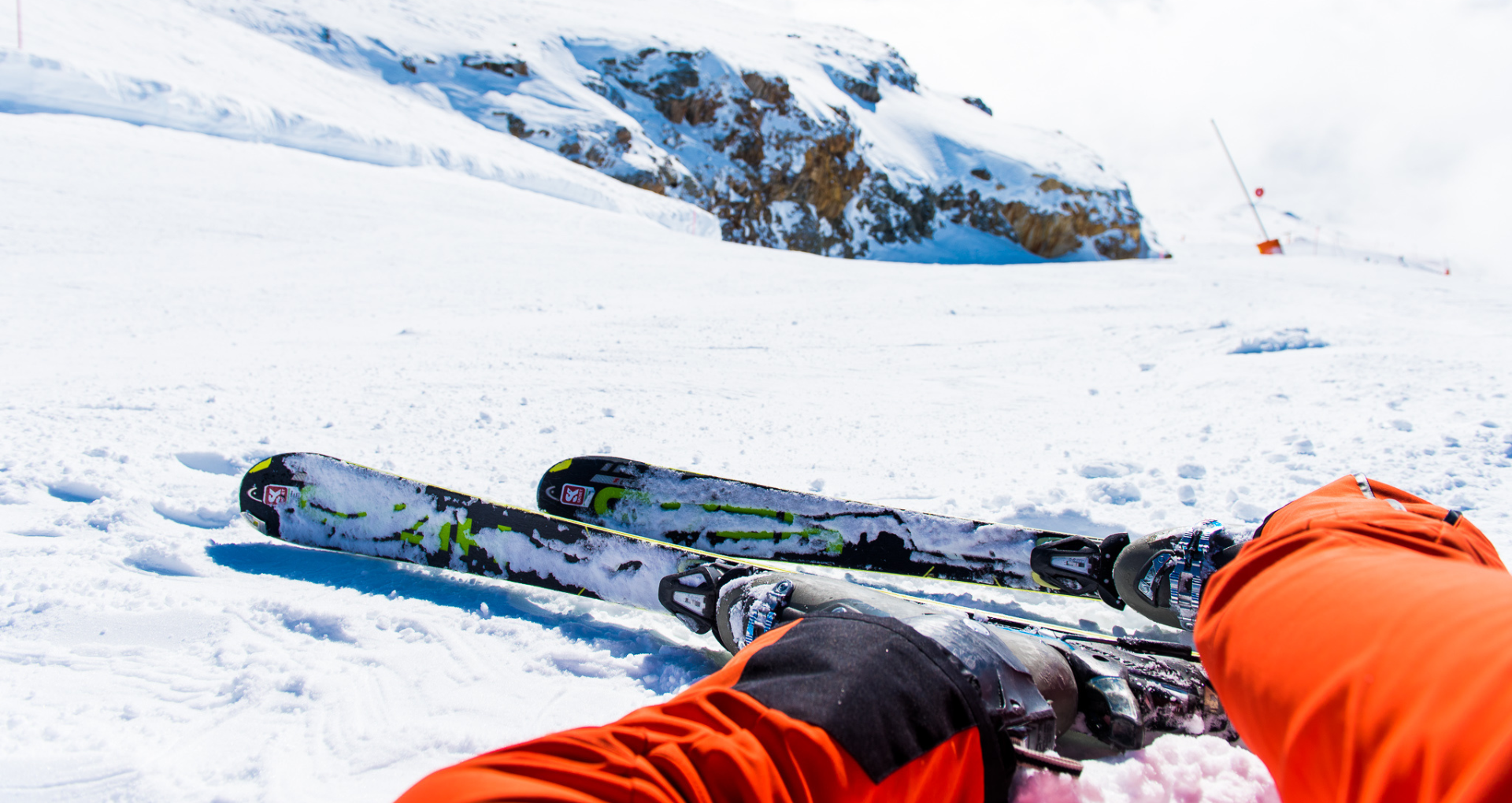 uitzicht op benen van persoon met oranje skibroek, liggend op besneeuwde piste