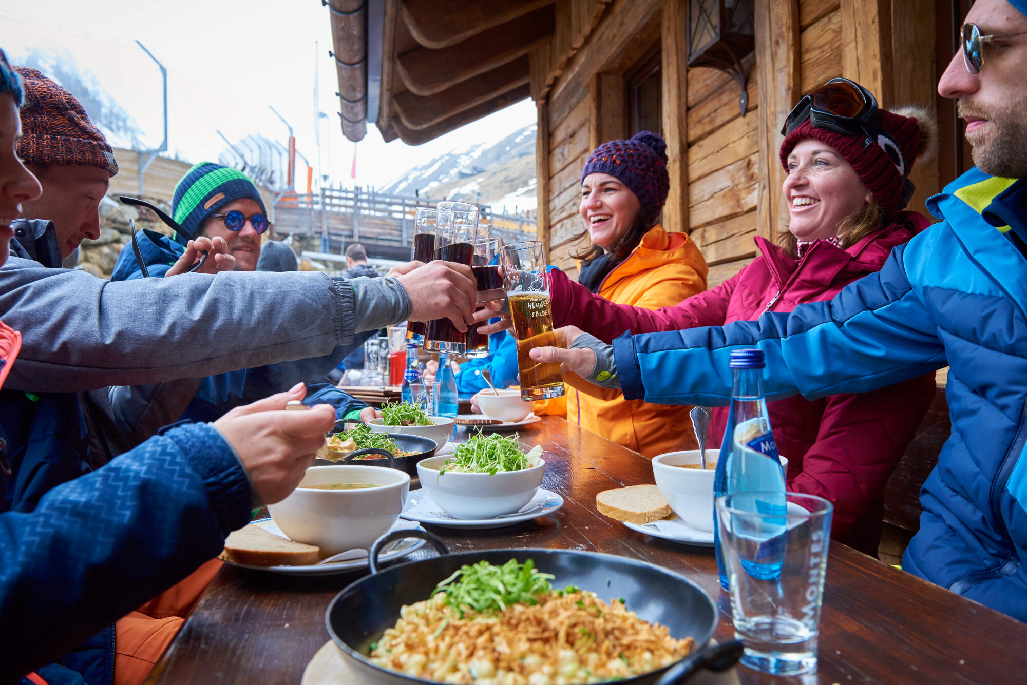groep mensen aan tafel met eten in skigebied proosten tegelijk en kijken elkaar lachend aan